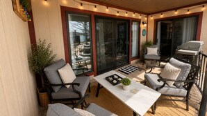 An outdoor patio with a table, chairs, string lights, and a grill.