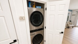 A laundry room with two stacked front-loading washing machines and a door leading to a living area.