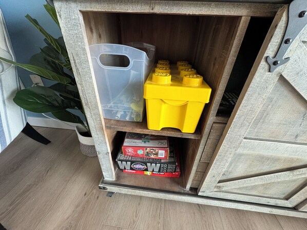 A wooden cabinet with a shelf containing a clear plastic container, yellow LEGO bricks, and a box of cereal.