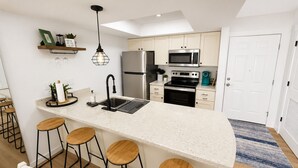 A modern kitchen with a central island, bar stools, a stainless steel refrigerator, a microwave, and a built-in oven.
