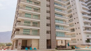 Un hotel de gran altura con varios balcones, una piscina con tumbonas y un cielo despejado.