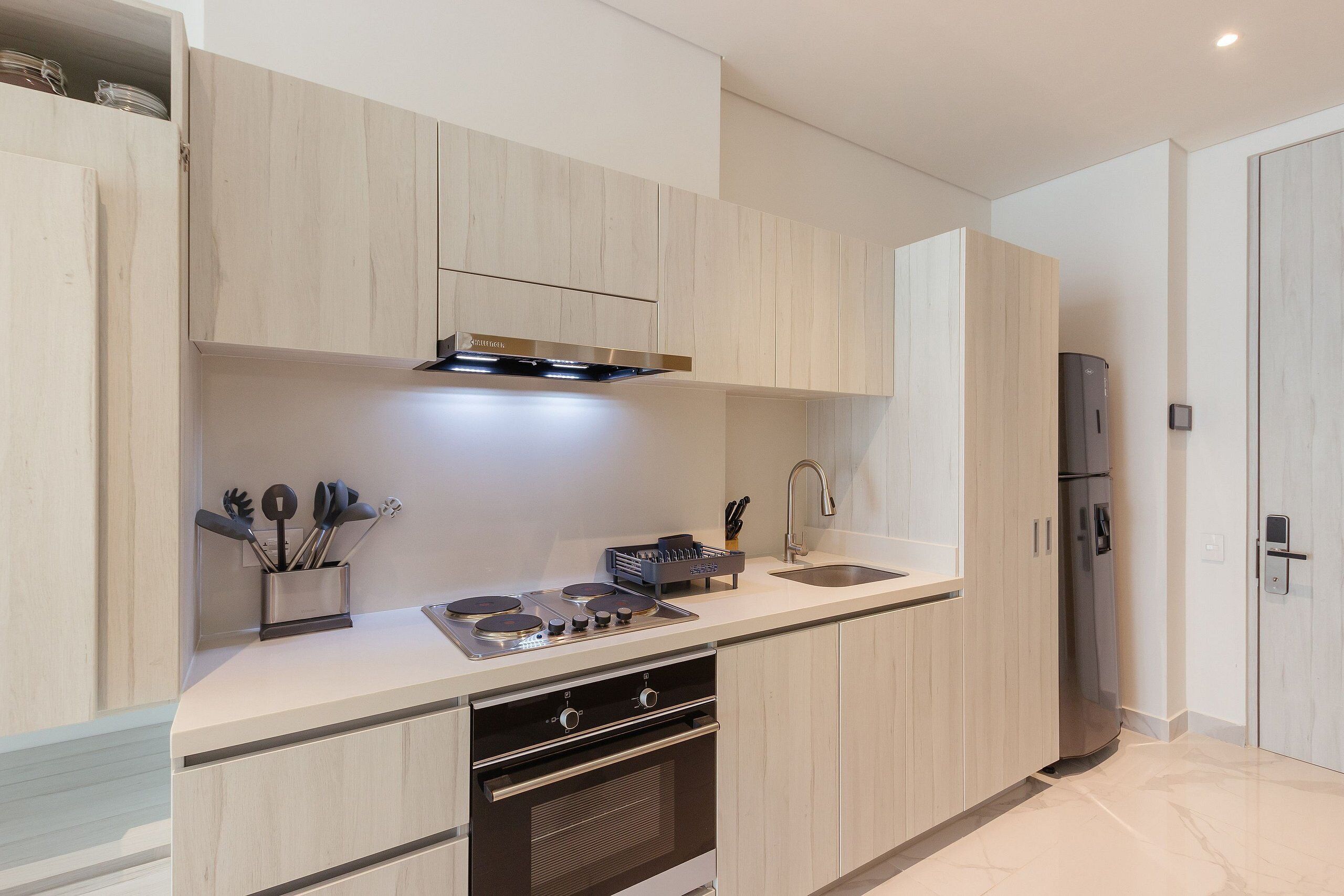 A modern kitchen with light wood cabinets, stainless steel appliances, and a built-in oven.