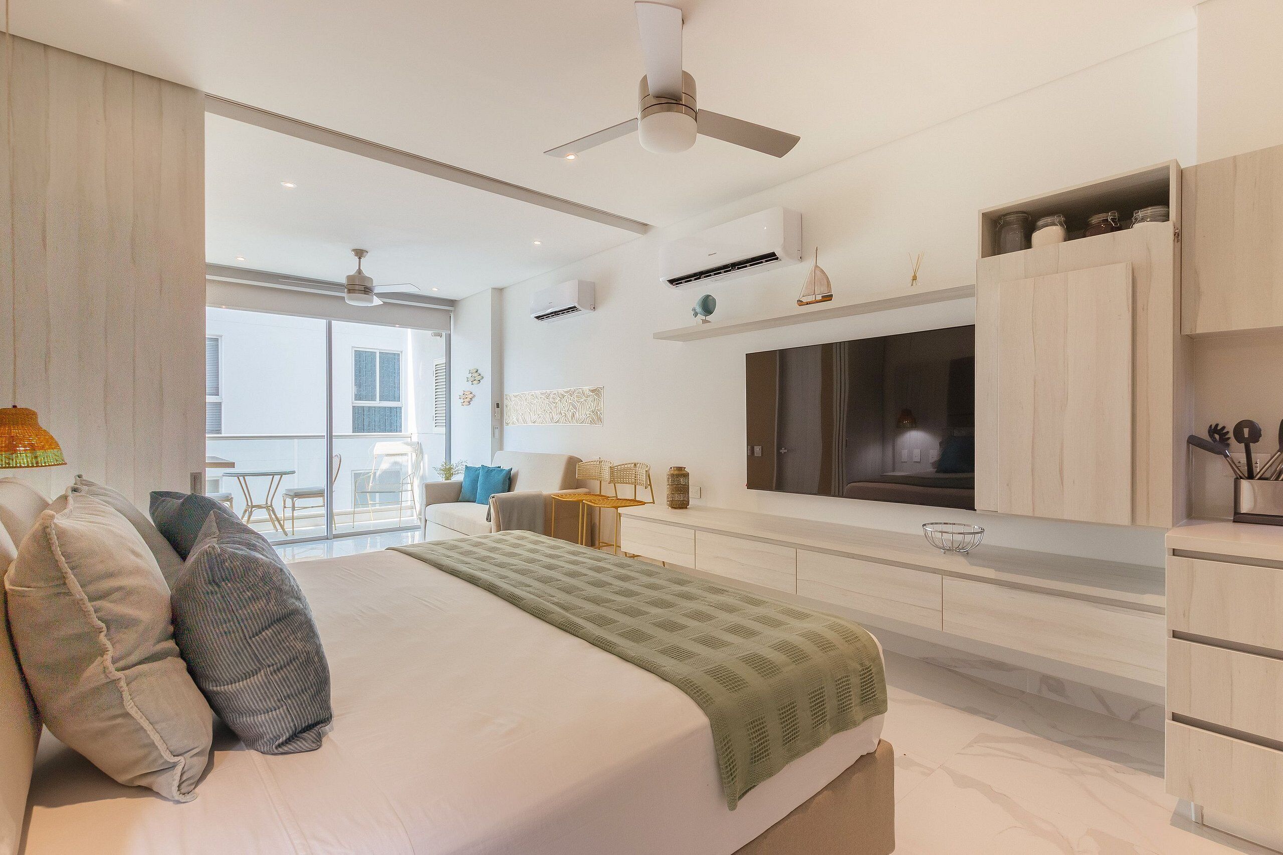 Un dormitorio moderno con una cama grande, un televisor montado en la pared y un balcón con vistas.