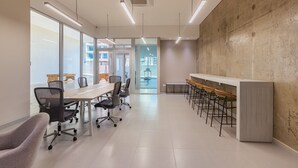 Una sala de conferencias moderna con una larga mesa, varias sillas, una zona de bar con taburetes y ventanas amplias que ofrecen luz natural.