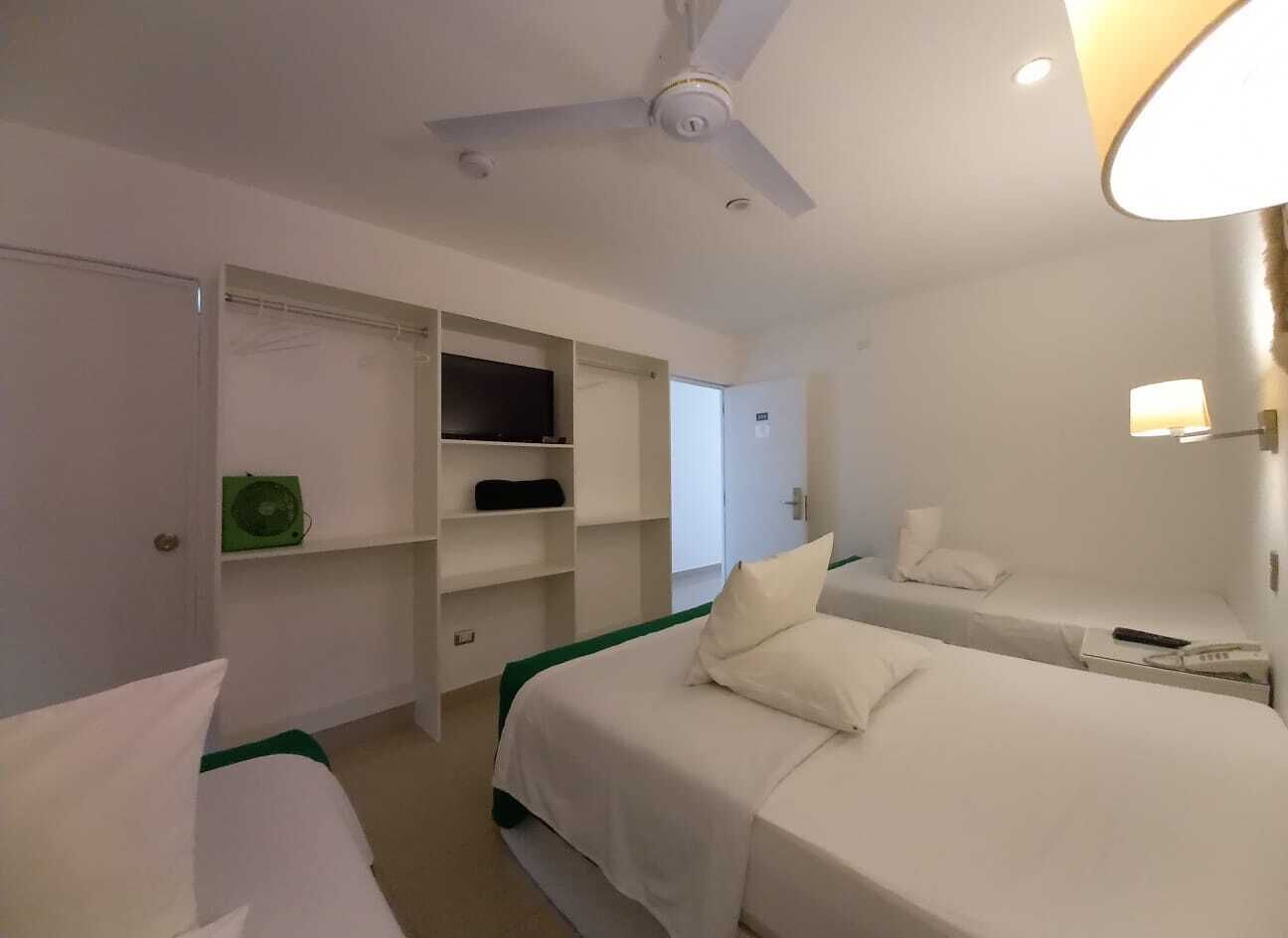 Ein Hotelzimmer mit zwei Betten, einem Deckenventilator, einem Kleiderschrank und einem Nachttisch mit Lampe.