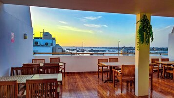 A terrace with wooden tables and chairs, overlooking a marina with boats.