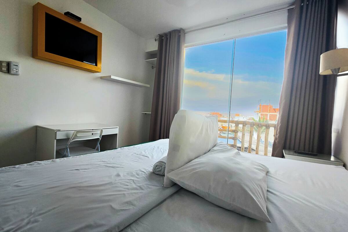 A hotel room with a bed, a desk, a television, and a view of the city.