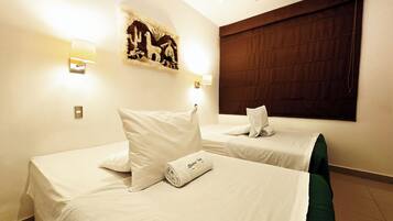 Habitación de hotel con dos camas, cada una con ropa blanca y almohadas. Hay una obra de arte colgada en la pared sobre las camas y un ventanal grande con persiana oscura.