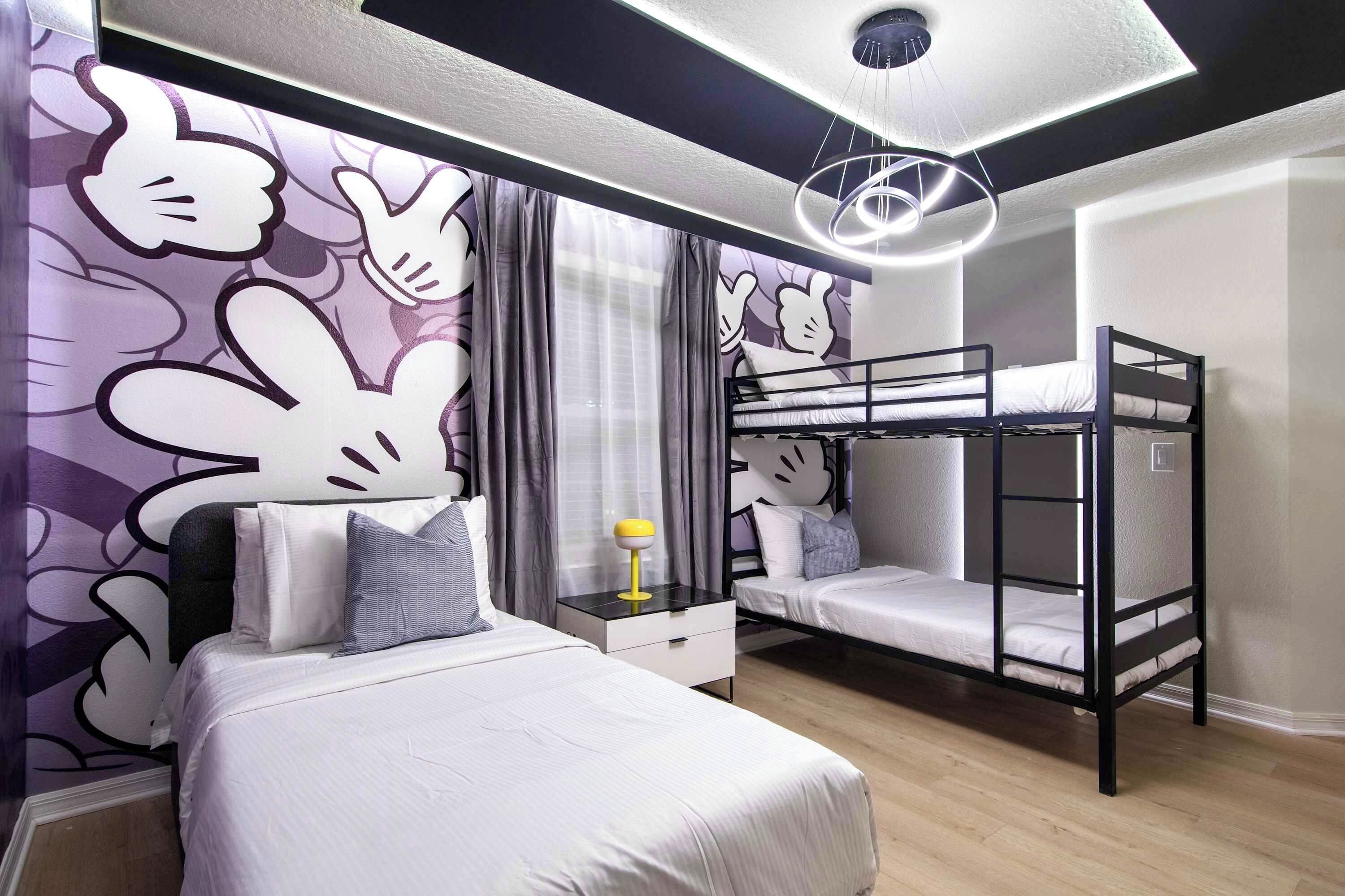 Un dormitorio con una litera, una cama individual, una mesita de noche y una pared con personajes de dibujos animados.