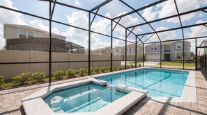 A swimming pool with a glass enclosure, surrounded by a brick patio and a view of residential buildings. - Escape to Luxury: Magical 10-bedroom Villa Near Disney World! (Davenport)