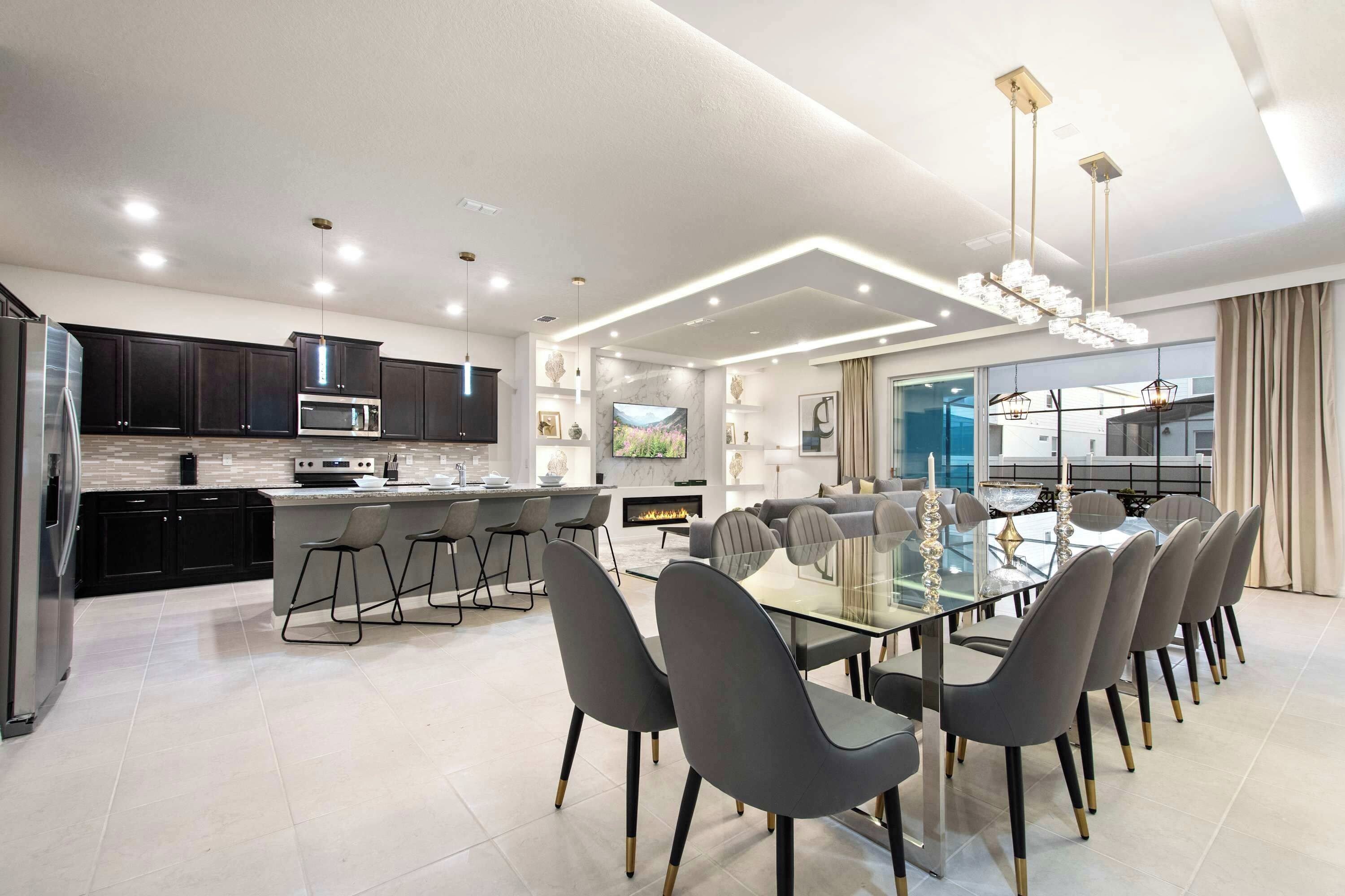 A modern kitchen with dark cabinets, a central island, and a dining area with a glass table and grey chairs.