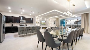 A modern kitchen with dark cabinets, a central island, and a dining area with a glass table and grey chairs. - Escape to Luxury: Magical 10-bedroom Villa Near Disney World! (Davenport)