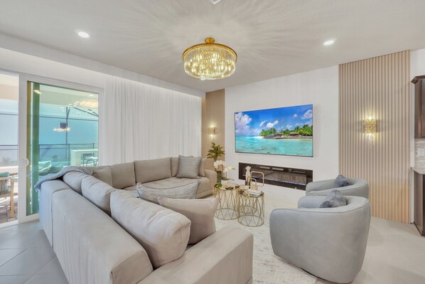 Una sala de estar moderna con un sofá modular, un sillón gris, un televisor montado en la pared y una chimenea.