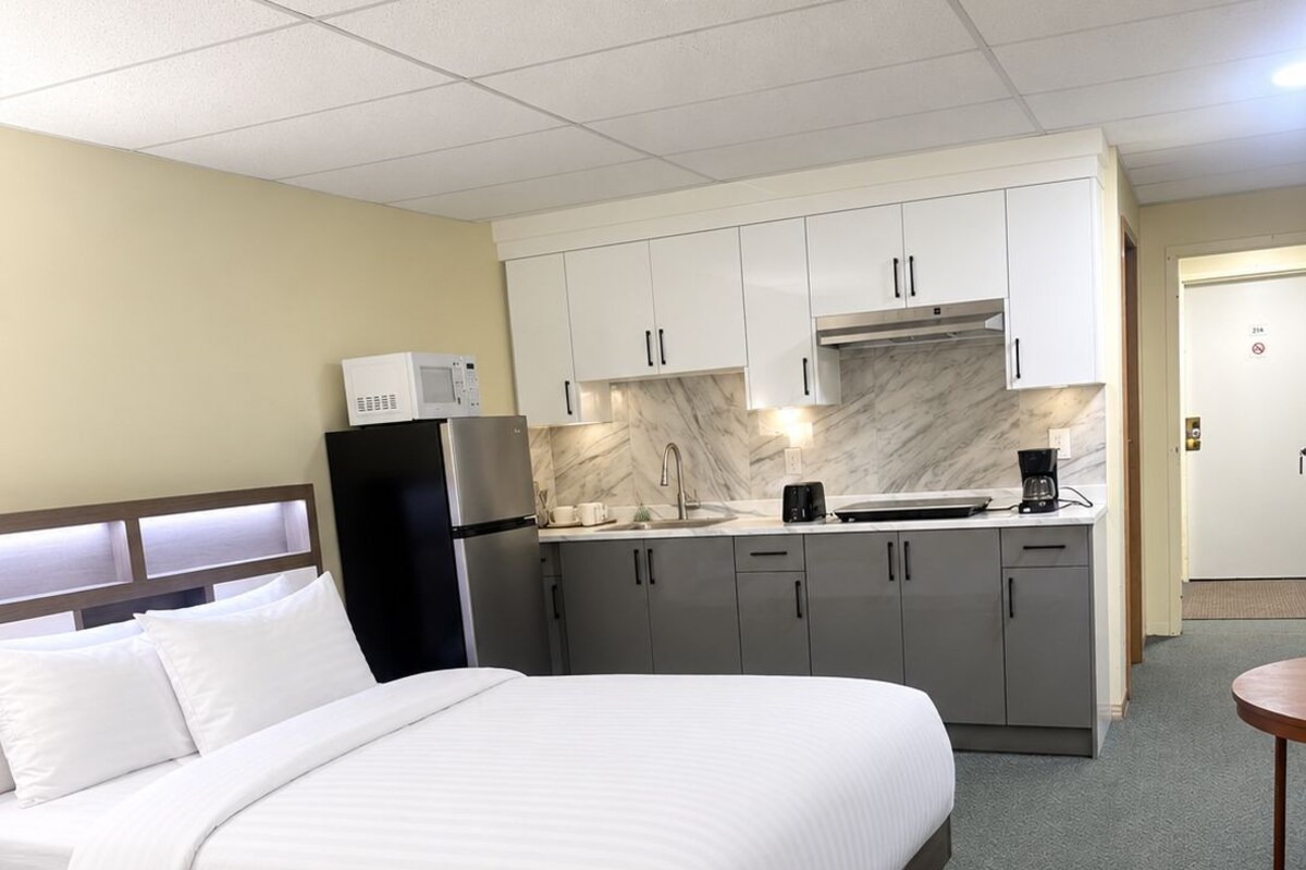 Quarto de hotel com cama, cozinha compacta e uma pequena mesa.