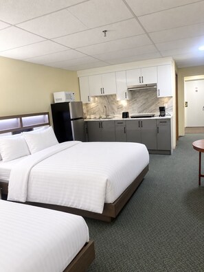 Hotellihuone, jossa on sänky, pieni keittiönurkkaus ja pieni pöytä.