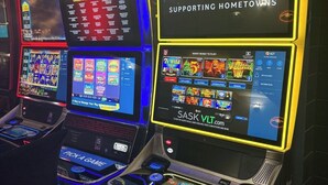 A row of slot machines with digital displays, one prominently displaying "SASK VLT" and "SUPPORTING HOMETOWNS". - Maple Creek Motor Inn (Maple Creek)