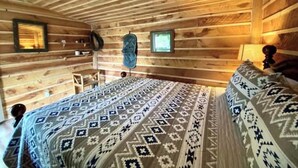 A wooden cabin room with a bed, a small table, and a chair. - Buffalo Bill Cabin At Mountain River Ranch (Ririe)