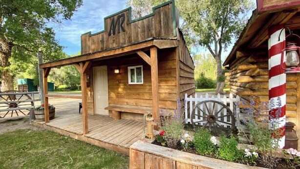 A rustic wooden building with a porch, a white picket fence, and a vintage lantern. - Buffalo Bill Cabin At Mountain River Ranch (Ririe)