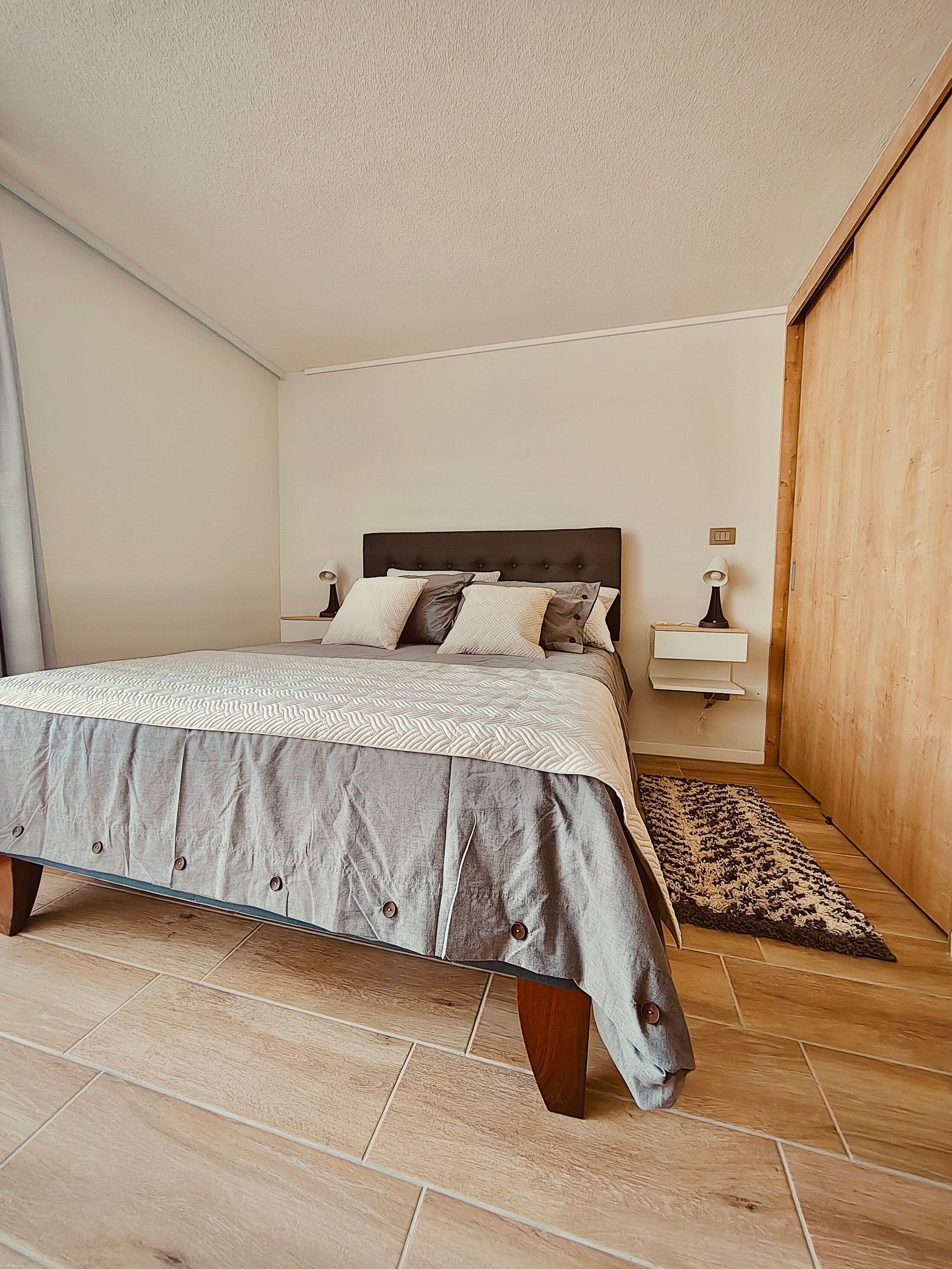 Une chambre à coucher avec un lit, des tables de chevet, un tapis et une porte en bois.