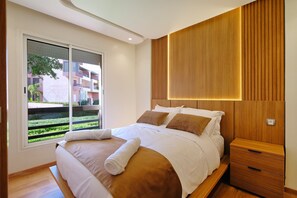 A modern bedroom with a large bed, wooden panel wall, and a view of a building through a window. - Calm and luxury (Marrakech)