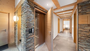 A modern hallway with wooden beams, stone accents, and a glass elevator door.