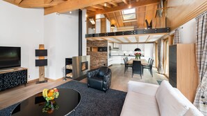 A modern living room with a black leather sofa, a white couch, a glass coffee table with fruit, a flat-screen TV, and a fireplace.