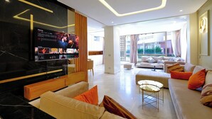 A modern living room with a large flat-screen TV, comfortable seating, and a view of the outdoors.