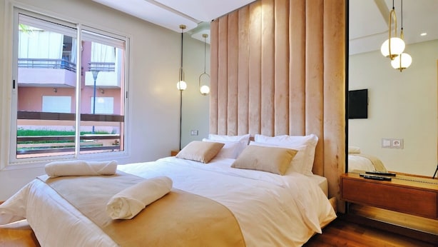 A modern bedroom with a large bed, a wooden headboard, and a balcony view.