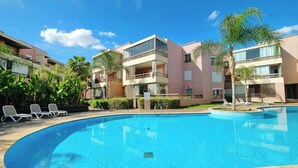 A swimming pool with lounge chairs, surrounded by multi-story buildings with balconies and palm trees.