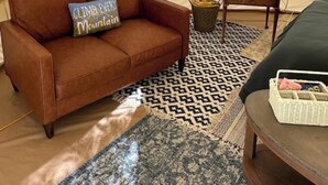 A tent interior with a brown leather sofa, patterned rugs, and a small table with a lamp and books.
