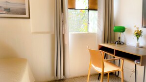 Una habitación con una cama, un escritorio con una silla, una lámpara de escritorio verde y un florero con flores.