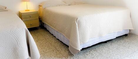 Un dormitorio con cama, mesita de noche, lámpara y un pequeño cuadro colgado en la pared.