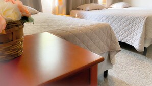 A hotel room with two beds, a wooden nightstand, a wicker basket with flowers, and a window with curtains.