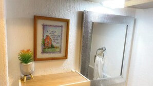 A bathroom with a framed quote on the wall, a small plant, and a mirror above a sink.