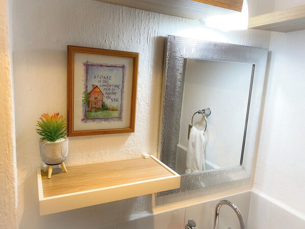 A bathroom with a framed quote on the wall, a small plant, and a mirror above a sink.