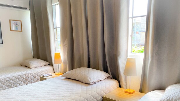 A hotel room with two beds, each with a white quilted bedspread and matching pillows. There are two bedside tables with lamps, and a framed picture on the wall.