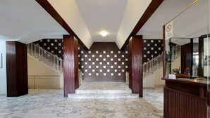 A marble-floored lobby with a staircase, wooden columns, and a reception desk.