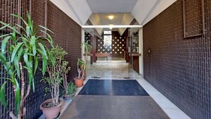 A hallway with a black mat, potted plants, and a patterned wall.