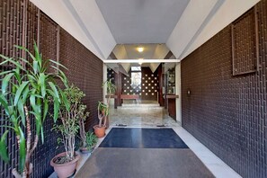 A hallway with a black mat, potted plants, and a patterned wall.