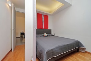 Een slaapkamer met een bed, een abstract schilderij in rood en een plafondlamp.