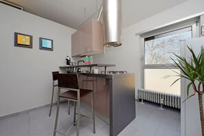 A modern kitchen with a bar area, a gas stove, and a window providing a view of trees. - Rome, Esquilino, apartment for 4 (Roma)