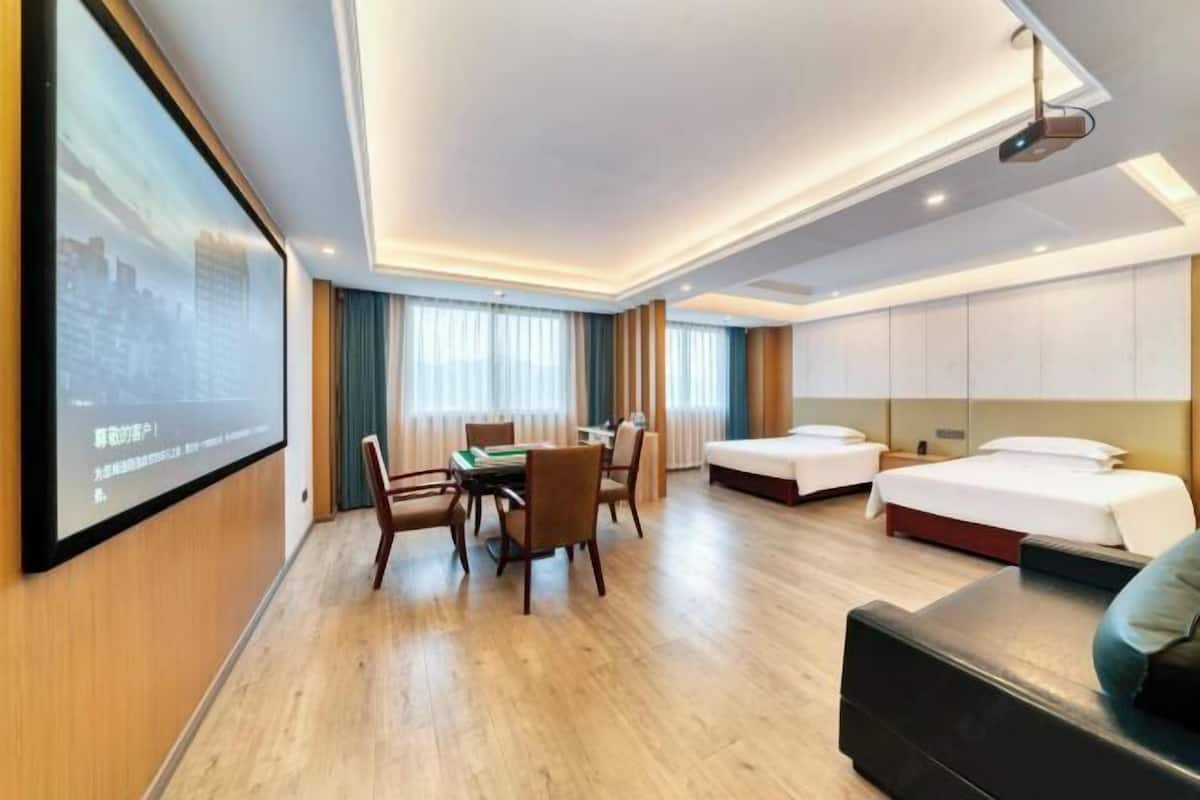 Une chambre d’hôtel avec un plancher en bois, une table à manger avec des chaises, deux lits, un canapé et un écran de projection fixé au mur.