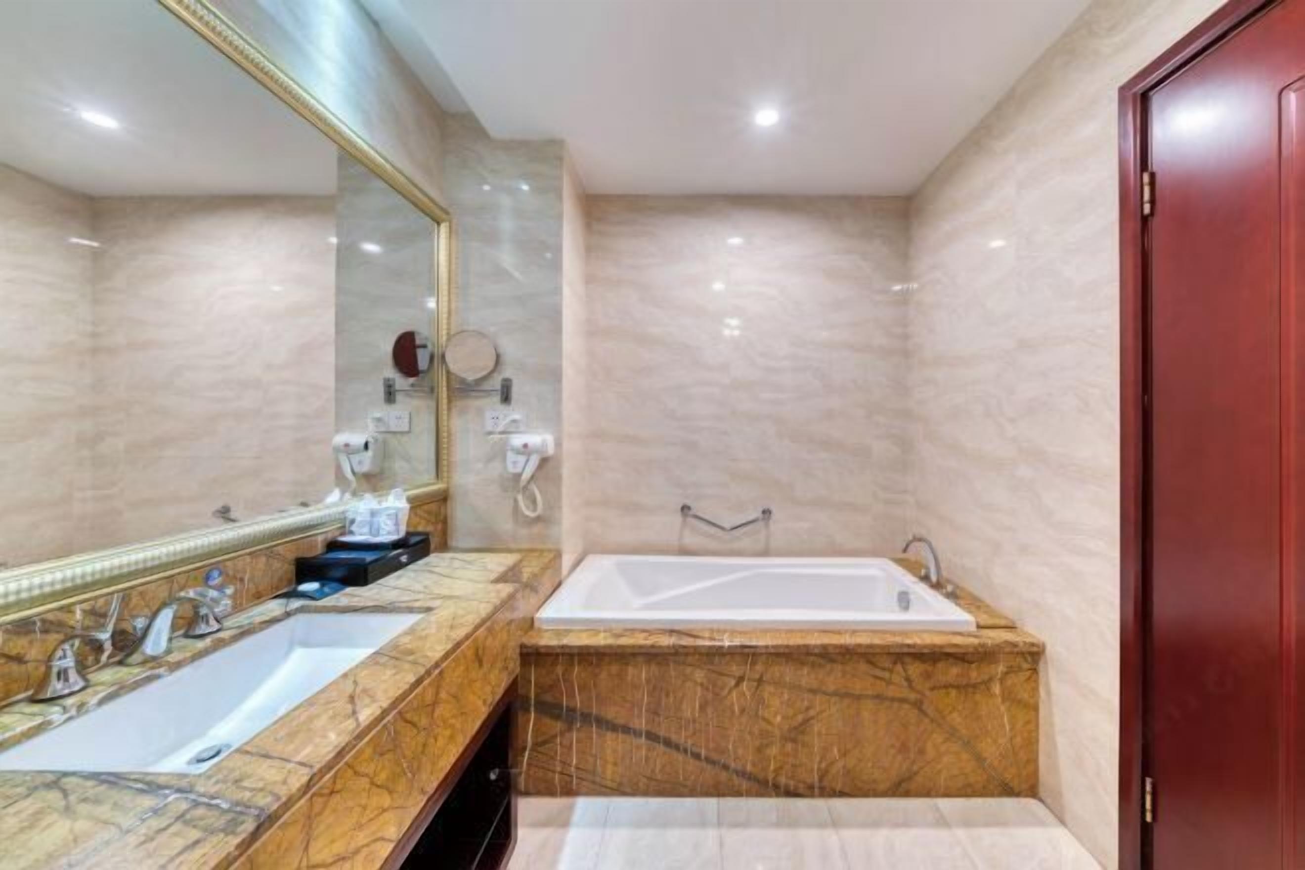 A bathroom with a marble vanity, a large mirror, a bathtub, and a red door.