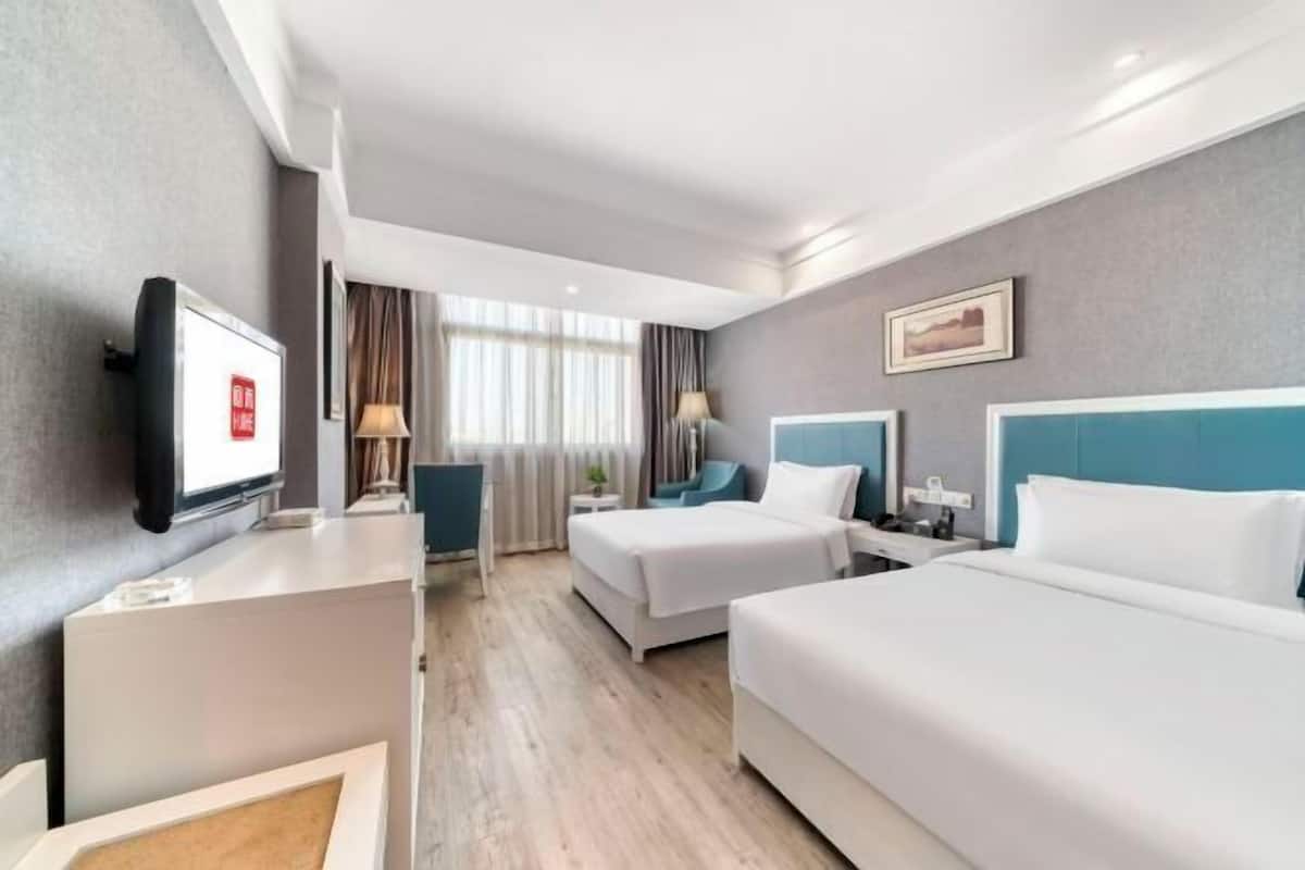 Une chambre d’hôtel avec deux lits, un bureau, une télévision et une fenêtre avec des rideaux.