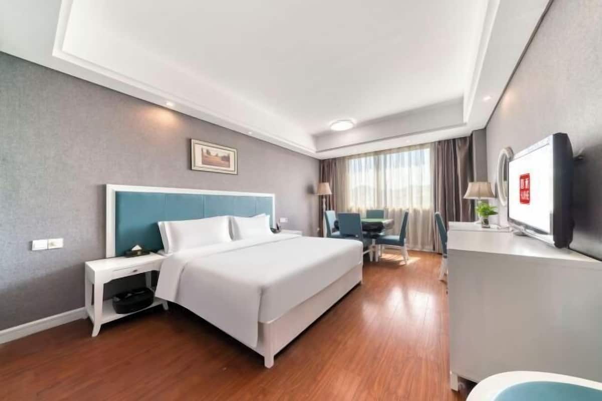 Une chambre d’hôtel équipée d’un lit, d’une table de chevet, d’un bureau, d’une chaise, d’une télévision et offrant une vue sur l’extérieur.