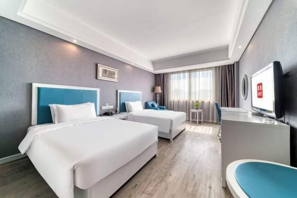 Une chambre d’hôtel avec deux lits, un bureau, une télévision et une fenêtre avec des rideaux.