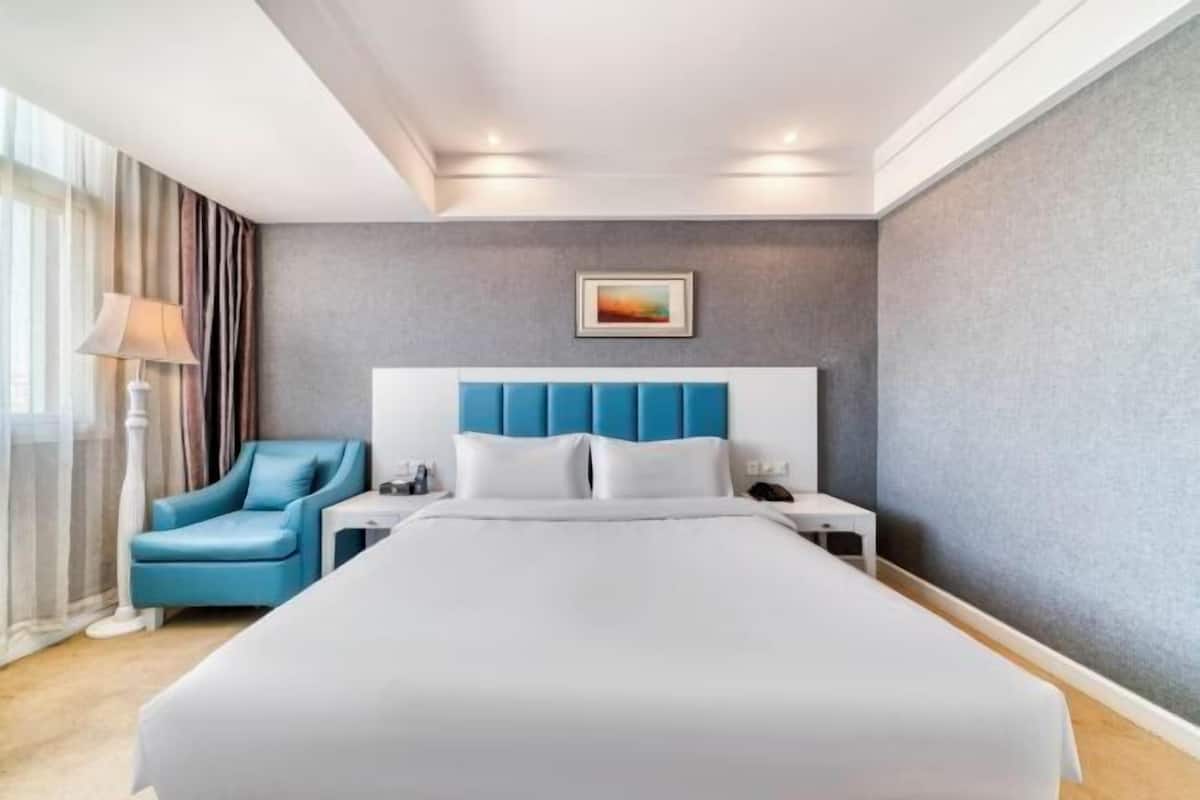 Une chambre d’hôtel avec un grand lit, un fauteuil bleu, une table de chevet et une commode.