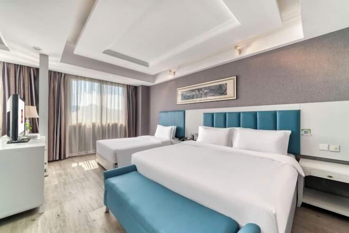 Une chambre d’hôtel avec deux lits, un bureau et une grande fenêtre avec des rideaux.