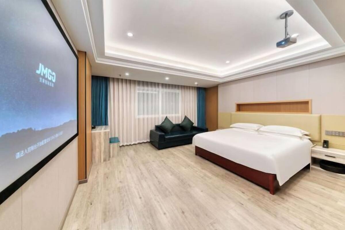 Une chambre d’hôtel moderne dotée d’un grand lit, d’un coin salon et d’un écran de télévision affichant le nom de l’hôtel.