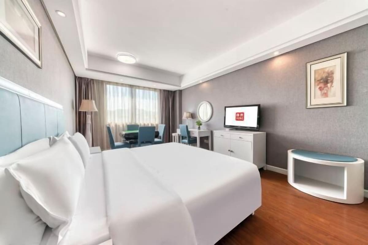 A hotel room with a large bed, a desk, a TV, and a seating area.
